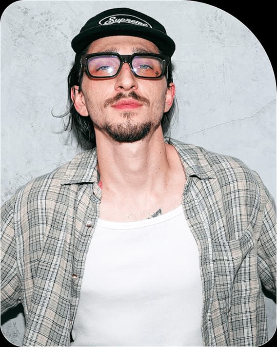 Hotel Ugly wearing a black cap, glasses and a checked shirt