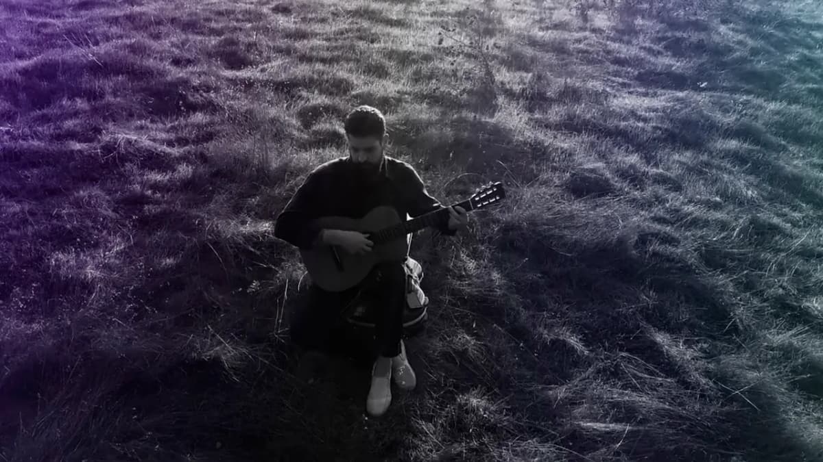 Jacob Montague playing guitar outdoors in a grassy field