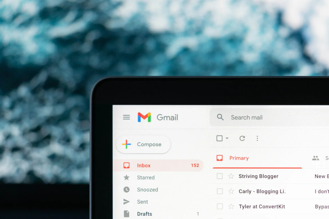 Close-up of a Gmail inbox on a laptop screen, showing 152 unread emails in the Primary tab, with a blurred blue background.